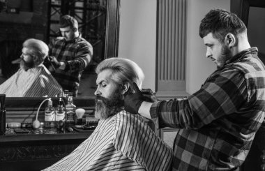 Yaşam tarzı. Usta berber saç stilini ve saç stilini kurutma makinesiyle yapıyor. Berber dükkanı kavramı. Genç hippi sakallı adam berber dükkanında saçını kesiyor. Profesyonel kuaförlük işi. Genç ve özgür.