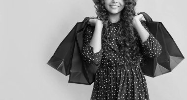 Kıvırcık saçlı gülümseyen kız sarı arka planda alışveriş torbaları tutuyor..