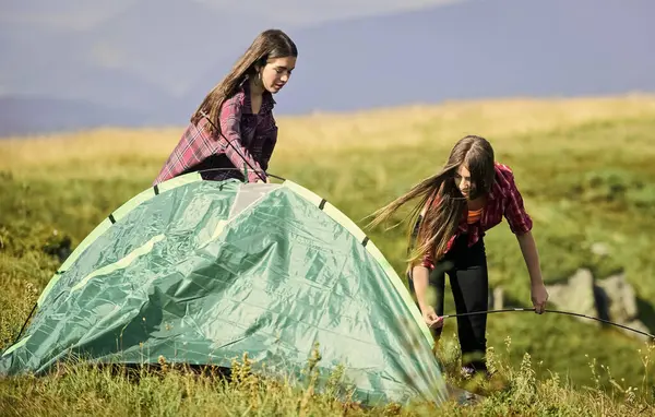 No care and no rush. mountain tourism camp. hiking outdoor adventure. family camping. reach destination place. two girls pitch tent. wanderlust discovery. friends spend free time together.