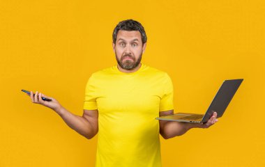 Şok adam stüdyoda online çalışıyor. İnternette bilgisayarlı ve telefonlu çalışan bir adamın fotoğrafı. Çevrimiçi çalışan bir adam sarıda yalnız çalışıyor. Adam çevrimiçi olarak arka plan üzerinde çalışıyor.