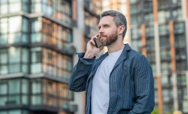 Sokakta cep telefonuyla konuşan bir adam, reklam. Adam cep telefonunu arıyor. Cep telefonundaki adamın fotoğrafı. Adamın dışarıda cep telefonu var..