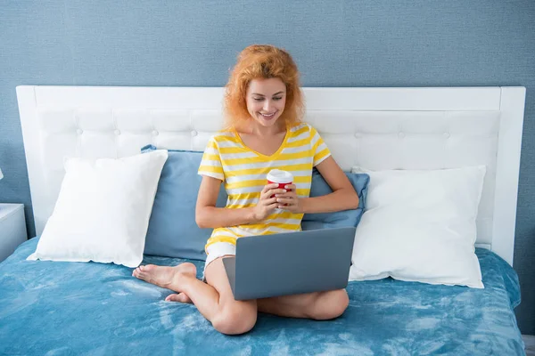 smiling girl freelancer with coffee work at home on laptop. freelancer girl work at home. home work for freelancer. girl in bed with laptop.