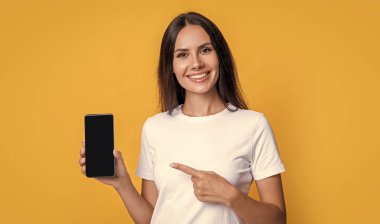 Mutlu kadın cep telefonunu işaret ediyor. Gülümseyen bir kadın mobil cihaz sunuyor. Mobil teknoloji. Mobil iletişim. Sunulan ürün, kopyalama alanı.