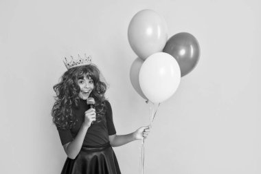 Sarı arka planda mikrofon ve parti balonu olan tacın içindeki mutlu çocuk..