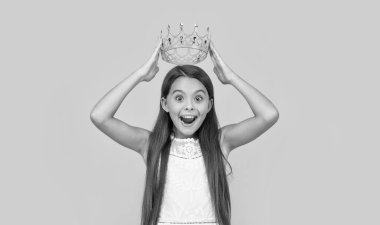 amazed teen girl in crown on yellow background.