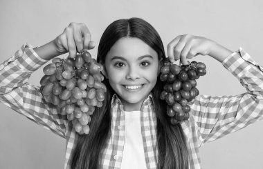 Sarı arka planda üzüm meyvesi olan mutlu genç çocuk..