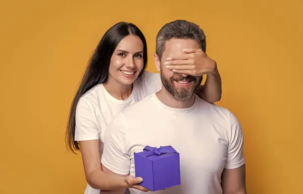 happy surprise couple with present in studio. holiday couple with present box. photo of couple with present for holiday surprise. mens day. couple with surprise present isolated on yellow background.