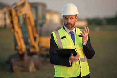 Miğfer takan ciddi bir amir. Yönetici adamın fotoğrafı. İnşaat alanındaki denetçi. Denetmen dışarıda..