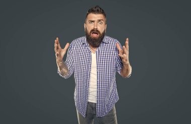 Şok olmuş sakallı adam gri arka planda kareli gömlek giyiyor..