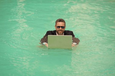 İş adamının yaz havuzunda uzaktan yüzerken çekilmiş fotoğrafı. Uzaktan kumandalı çalışan iş adamı. Yüzme havuzunda uzaktan kumandalı çalışan iş adamı. Uzaktan kumandalı iş adamı.