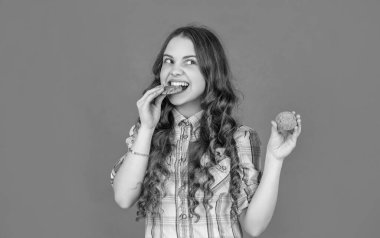 hungry teen girl with oatmeal cookies on orange background.