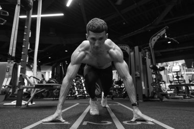 Çömelme pozisyonu almış, dizlerinin üstüne çökmüş ve elleri spor salonunda başlangıç çizgisinde. Koşmak için formda bir adam başlangıç pozisyonunda. Spor salonunda atlet eğitimi. Spor salonunda koşu antrenmanı. Spor ve zindelik.