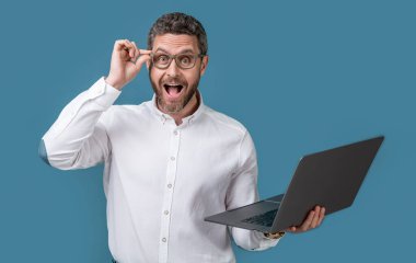 surprised businessman freelance in studio. businessman freelance with computer. businessman freelance holding laptop. businessman freelance isolated on blue background.