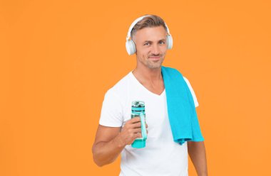 Mutlu adam şişeyi sağlıklı bir yaşam için tutuyor. Sağlıklı yaşam tarzı için spor şişesi olan adam sarıda izole edilmiş. Spor yaşam tarzını korumak için elinde şişe tutan adam. Eğitimden sonra havluyla şişesi olan adam.