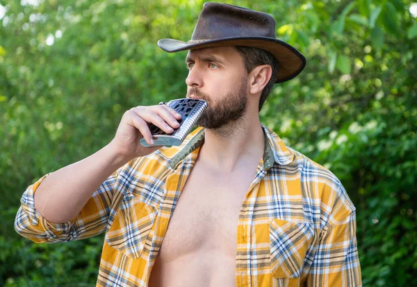 western man drink whiskey flask wear checkered shirt. photo of western man with whiskey flask. western man with whiskey flask. western man with whiskey flask outdoor.