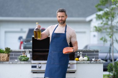 Dışarda somon balıklı bbq-man var. Önlüklü somon balıklı bbq adam. BBC-Man 'in somon balıklı fotoğrafı. Somon balıklı bbq man..