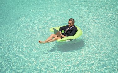 İnsan ticareti yapar ve bilgisayarla rahatlar. İnsan ticaretinin fotoğrafı ve havuzda rahatlamak. Tüccar işi ve rahatlama. Adam tüccar işi ve yüzme havuzunda rahatlama.