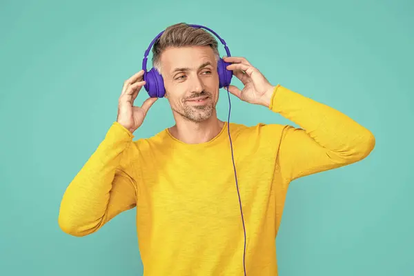 photo of smiling man listen music in headphones. man listen music in headphones isolated on blue. man listen music in headphones at studio. man listen music in headphones on background.