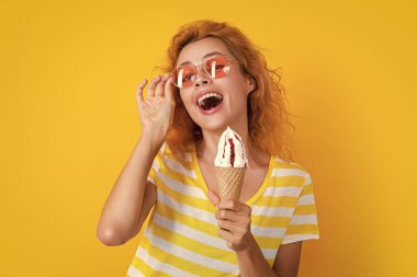 Stüdyoda dondurmalı neşeli kız. Arka planda dondurma külahı olan kız. Yazın külahta dondurmalı bir kızın fotoğrafı. Dondurmalı kız sarıda izole edilmiş..