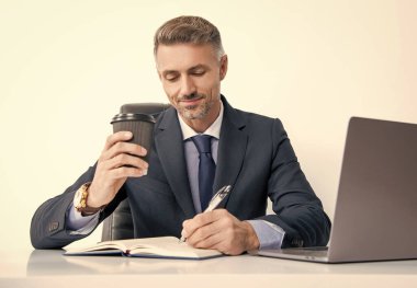 Olgun bir ofis çalışanı iş ofisinde yazı yazıyor ve kahve içiyor..