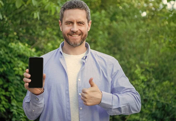 photo of man presenting smartphone, thumb up. man presenting smartphone. man presenting smartphone outdoor. man presenting smartphone screen with copy space.