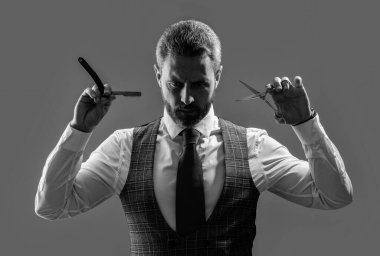 Yakışıklı, tıraşsız kuaför bıçak ve makas gri arka planda izole edilmiş. Adam kuaförle tıraş olur ve saç keser. Kuaför stüdyosunda berberlik yapan bir adam. Sakallı kuaför..