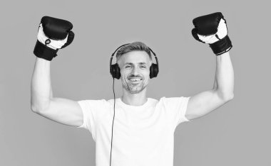 Stüdyoda boks eldivenli mutlu adam boksörü. Spor eldivenli bir boksör kulaklık takıyor. Boks eldiveni giymiş boksör adamın fotoğrafı. Boks eldivenli adam mavi üzerine izole edilmiş..