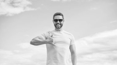 cheerful man in yellow shirt and sunglasses outdoor on sky background. thumb up.