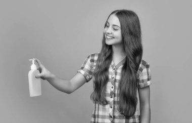 Sarı arka planda sıvı sabun şişesi olan gülümseyen çocuk..