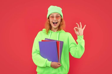 Öğrenci kız öğrencinin fotoğrafı kitap tutuyor, tamam. Okul eğitimi almış bir kadın öğrenci. Kırmızı arka planda izole edilmiş bir okul öğrencisi. Stüdyodaki kız öğrenci..