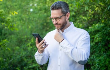 Gülümseyen iş analisti internette çalışıyor. İş analisti açık havada telefonla çalışıyor. İnternette çalışan iş analisti. İnternet üzerinde çalışan iş analistinin fotoğrafı.