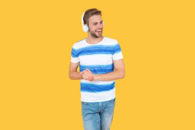 Neşeli adam sarı arka planda izole edilmiş kulaklıklarıyla müzik dinliyor. Adam rahatlar stüdyoda müzik dinler. Adam müzik dinlemek için kablosuz kulaklıklarını kullanıyor. Erkekler canlı müzik dinlemeyi sever..