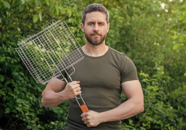 Adam barbekü ızgarasını beklesin. Dışarıda ızgara yapan adam. Barbekü aletli adam. Mangallı adamın fotoğrafı..