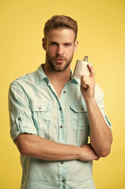 Adam stüdyo arka planında parfüm tutuyor. Erkek parfümünün görüntüsü. Erkek parfümü. Erkek parfümü sarı renkte tutar..
