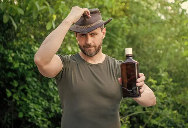 カウボーイはウイスキーを提供してる ウィスキーボトルを持ったカウボーイ ウイスキー アウトドアのカウボーイ ウイスキーとカウボーイの写真 — ストック写真