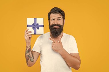 Sakallı adam hediye kutusunu stüdyoda, işaret parmağıyla tutuyor. Sakallı adam hediye kutusunu arka planda tutuyor. Sakallı adamın hediye kutusundaki fotoğrafı. Sakallı adam, hediye kutusunu sarıda sakla..