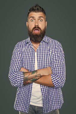 Şaşırmış sakallı adam gri arka planda kareli gömlek giyiyor..