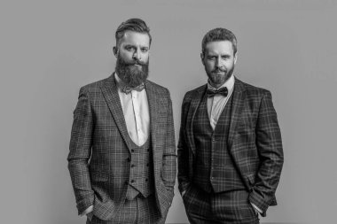 Stüdyoda smokinli iki adam. Smokinli adamlar arka planda. Smokinli adamların fotoğrafı var. Smokinli adamlar griden izole edilmiş..