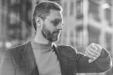punctual man check time on wristlet watch outside. photo of punctual man check time on watch. punctual man in jacket check time outdoor. punctual man check time in the street.