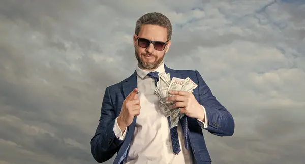 riches of man hold money on sky background. riches of man with money outdoor. riches of man with money in suit. riches photo of man with money.