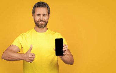 Stüdyoda akıllı telefon uygulaması gösteren bir adam, kopyalama alanı. Akıllı telefon uygulaması gösteren bir adamın fotoğrafı. Akıllı telefon uygulaması gösteren adam sarıda izole edildi. Adam arka planda akıllı telefon uygulaması gösteriyor.