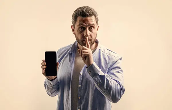 secret man showing phone app isolated on studio background. man showing phone app in studio. showing phone app. photo of man showing phone app.