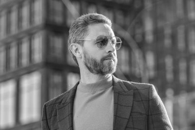 Havalı adam dışarıda güneş gözlüğü takıyor. Ceket giyen şık bir adamın fotoğrafı. Dışarıda ceketli şık bir adam var. Sokakta şık bir adam.