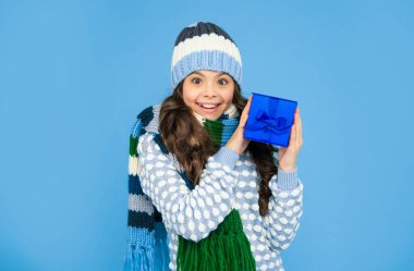 surprised child in knitwear hold box. kid with present. teen girl on blue background. winter holidays.