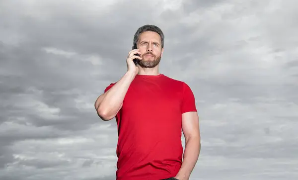 man has phone talk outdoor. man has phone talk wearing red tshirt. photo of man has phone talk. man has phone talk on sky background.