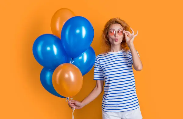 positive woman with birthday balloon in sunglasses. happy birthday woman hold party balloons in studio. woman with balloon for birthday party isolated on yellow background.