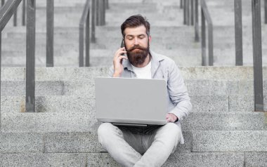 Adamın dışarıda görüntülü telefon bağlantısı var. Adamın merdivenlerde online video bağlantısı var. Adamın bilgisayarında çevrimiçi video bağlantısı var. Adamın dışarıda online video iletişimi var..