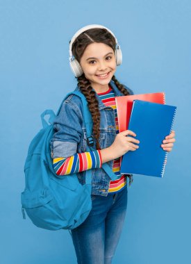 Happy teen girl listening to audio lesson blue background. Teenager listening to audiobook in headphones. Listening skills. School education.
