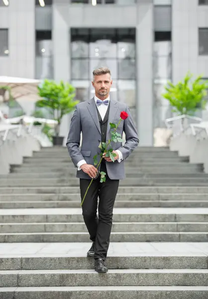 elegant man in tuxedo. man wearing tuxedo bowtie outdoor. caucasian tuxedo man with red rose.