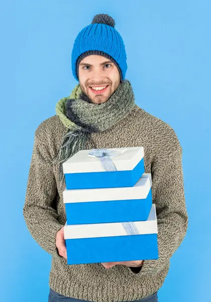 happy man hold present box isolated on blue background. man hold present box in studio. man hold present box for christmas holiday. man in winter clothes hold present box.
